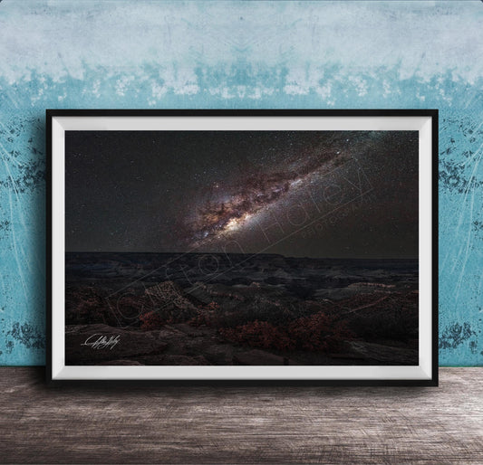 The image is a framed photograph of a night sky with a galaxy, placed on a wooden surface against a blue wall.