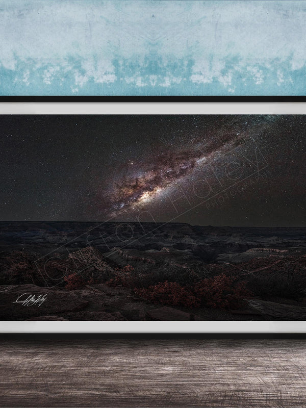 The image is a framed photograph of a night sky with a galaxy, placed on a wooden surface against a blue wall.