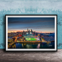A framed aerial view of a city skyline at night, with a brightly lit stadium and surrounding buildings.
