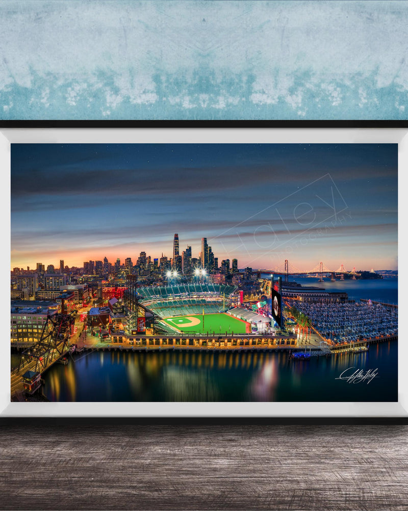 A framed aerial view of a city skyline at night, with a brightly lit stadium and surrounding buildings.