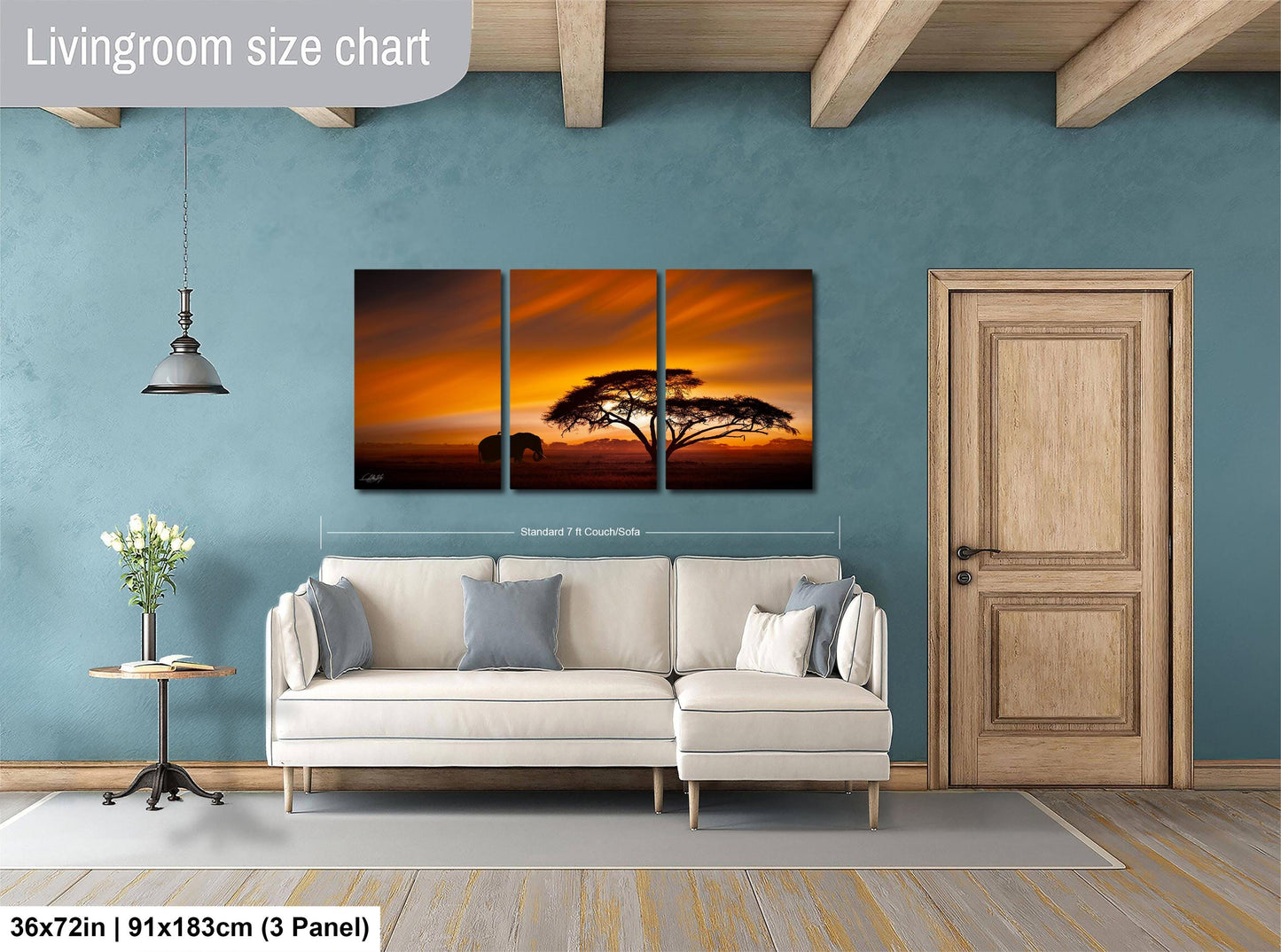 The image is a living room with a large wall art depicting a sunset over a savanna landscape. The wall art is divided into three panels, with the largest panel spanning approximately 36 inches by 21 inches. The smaller panels are smaller in size, with one panel measuring approximately 11.85 inches by 3.25 inches and another measuring approximately 11.85 inches by 3.25 inches. The room also includes a white sofa, a wooden door, and a small table with a vase of flowers.