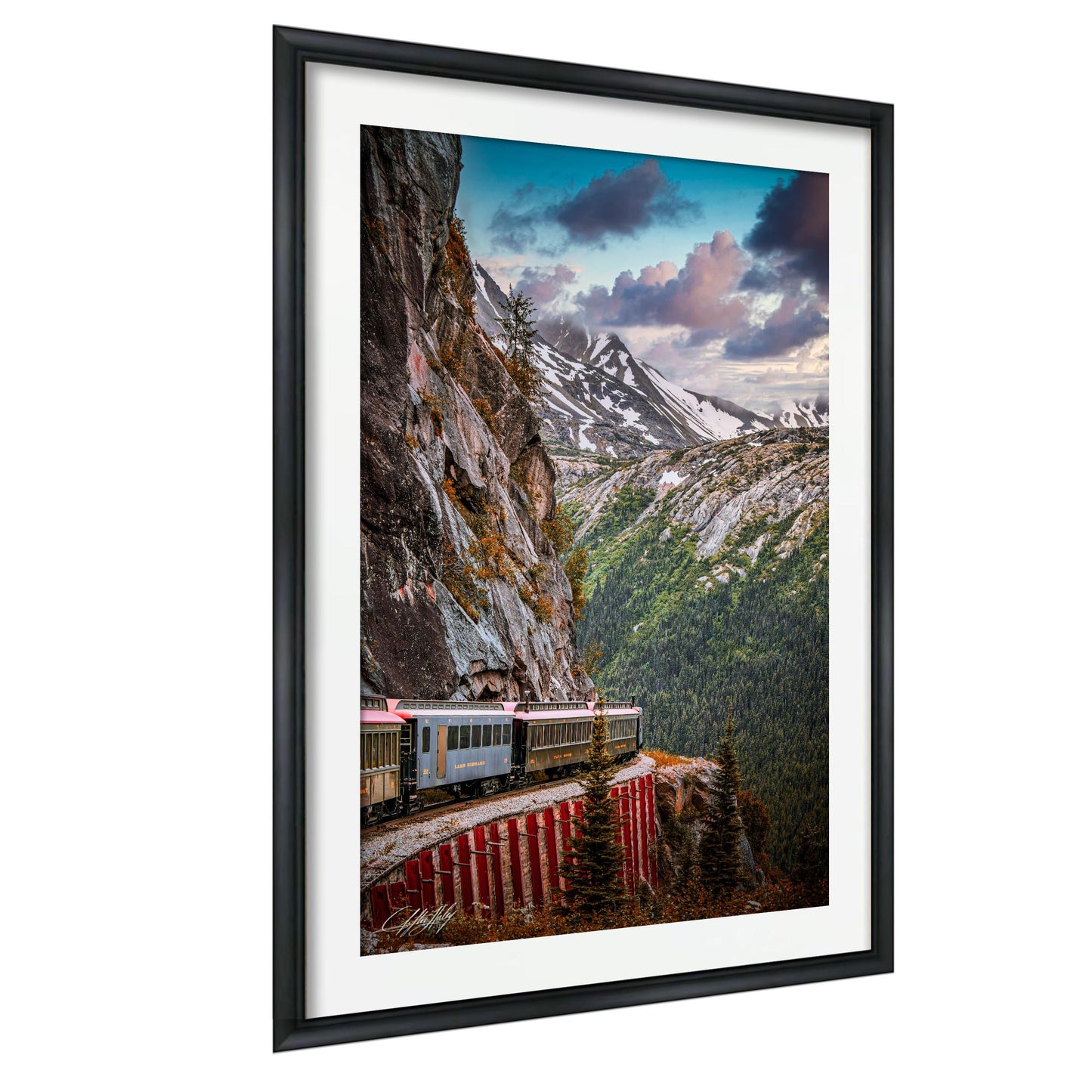 A framed photograph depicting a train traveling along a winding track that runs along the side of a steep, rocky mountain.