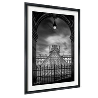 A black and white photograph of the Louvre Museum in Paris, France, with the iconic glass pyramid structure of the museum prominently featured.