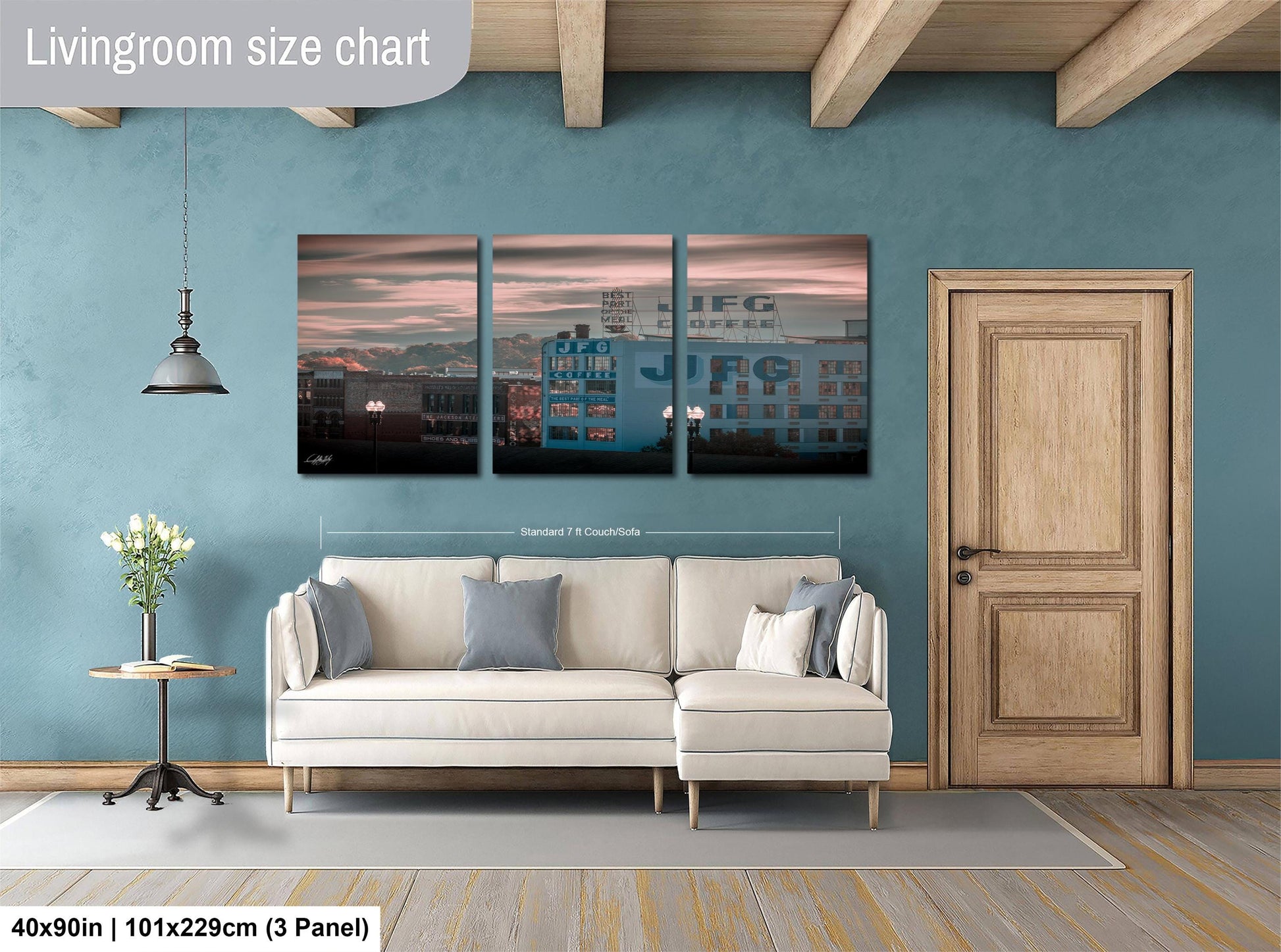 The image is a living room with a white sofa and a wooden door. Above the sofa, there is a triptych of paintings depicting a cityscape with buildings and a sunset. The paintings are framed and hung on the wall.