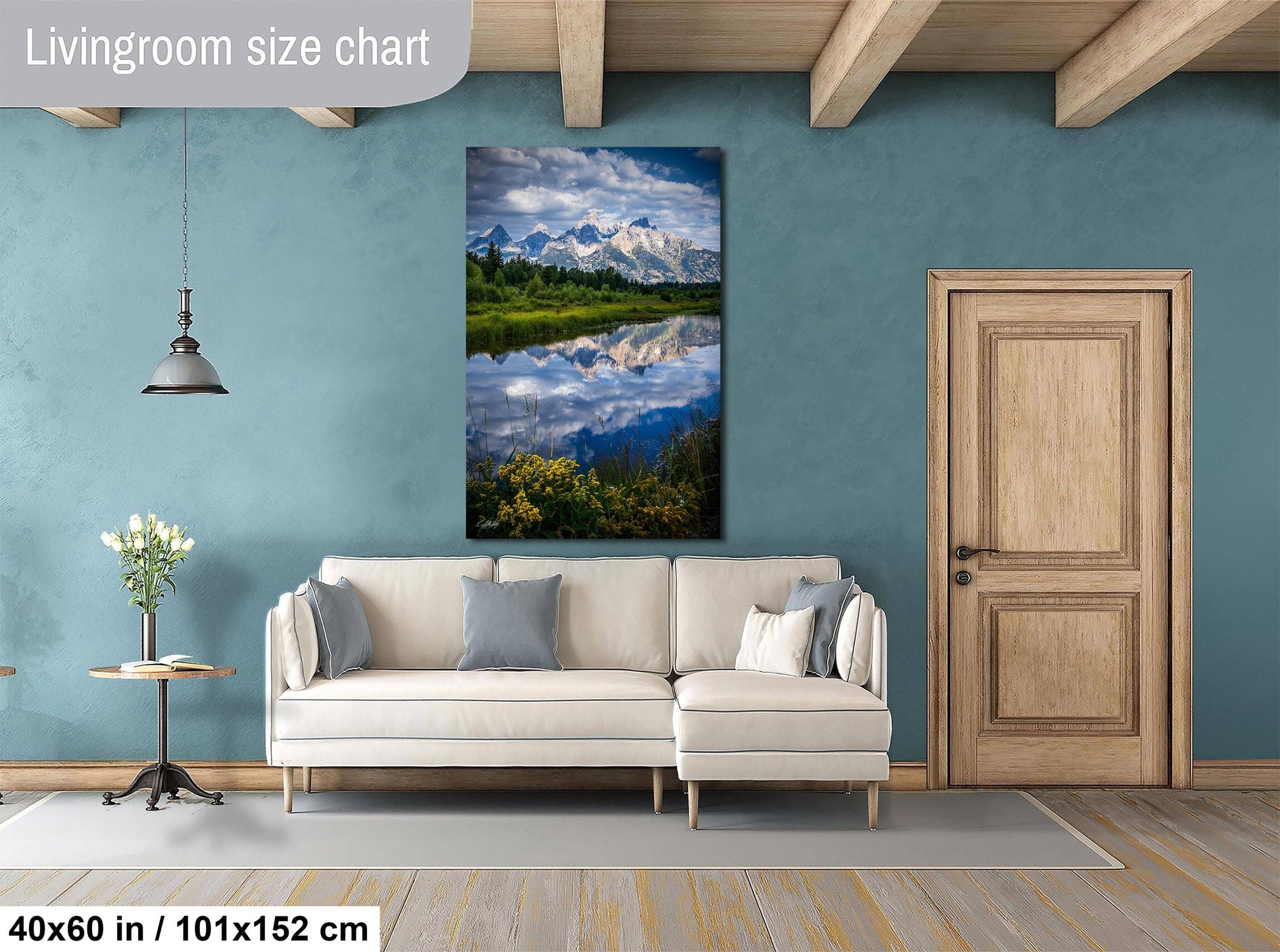 a living room with a large painting of a serene landscape hanging on the wall, featuring a lake and mountains reflected in the water. The room has a white sofa and a wooden door, creating a cozy and inviting atmosphere.
