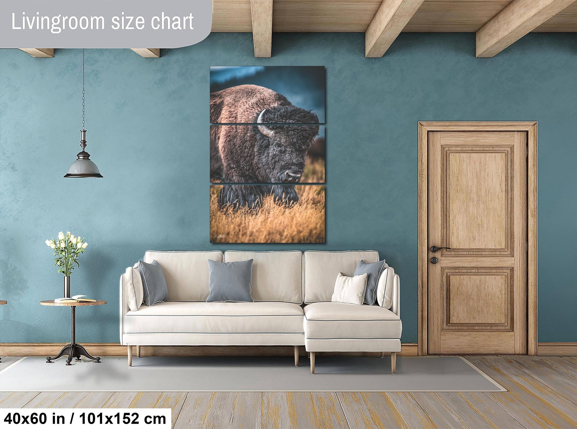 The image is a living room with a large painting of a bison on the wall, a white sofa, a wooden door, and a small table with a vase of flowers.