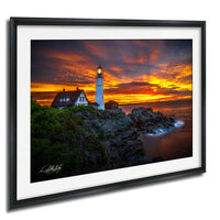 A framed photograph depicting a lighthouse on a rocky cliff at sunset, with a vibrant sky and ocean in the background.