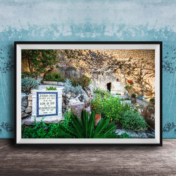 A framed photograph depicting a stone wall with a sign that reads "JESUS CHRIST" and "SON OF GOD". The wall is surrounded by lush greenery, including plants and trees.