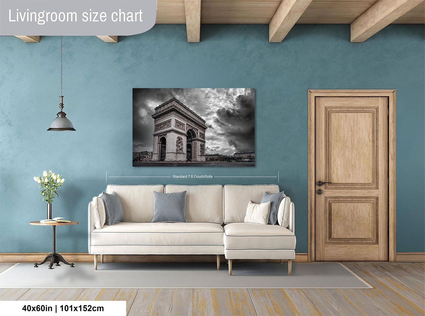 a living room with a large wall-mounted painting of the Arc de Triomphe in Paris, France. The painting is framed and hangs above a white sofa with two throw pillows. The room has a wooden door and a small table with a vase of flowers. The wall is painted a light blue color, and the floor is covered with a gray rug.