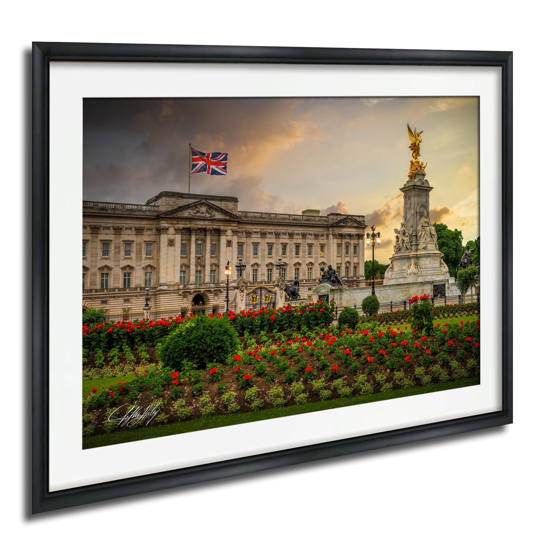 A framed photograph of Buckingham Palace in London, England, with the Union Jack flag flying in the background and a statue of a golden angel on a pedestal.