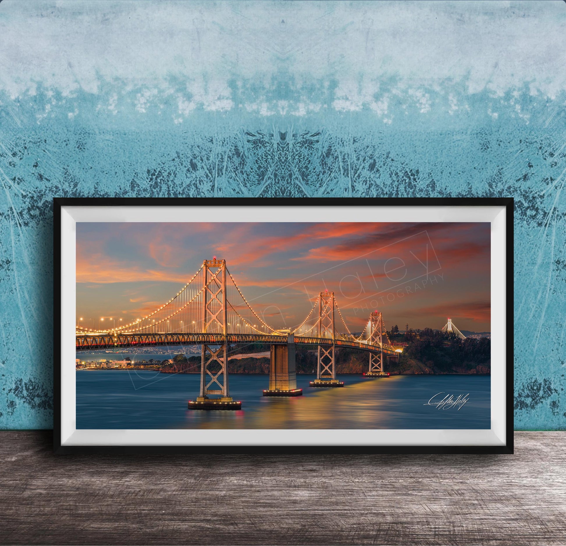 A framed photograph of the Golden Gate Bridge at sunset, with the bridge illuminated and its towers and suspension cables glowing against the colorful sky.