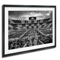 A black and white photograph of a football stadium with a large crowd of spectators, a large scoreboard, and a marching band performing on the field.