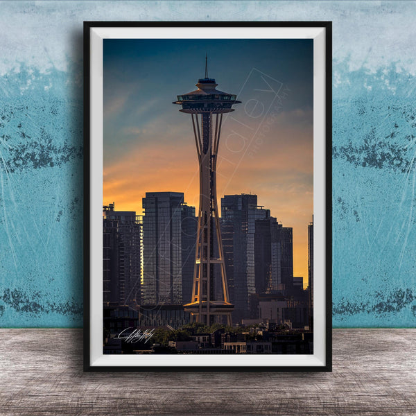 A framed photograph of the Space Needle in Seattle, with the city skyline in the background at sunset.