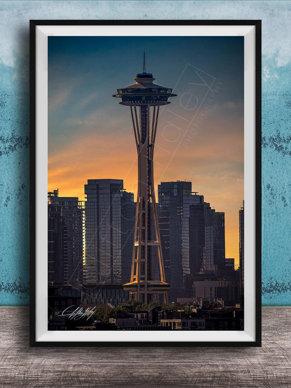 A framed photograph of the Space Needle in Seattle, with the city skyline in the background at sunset.