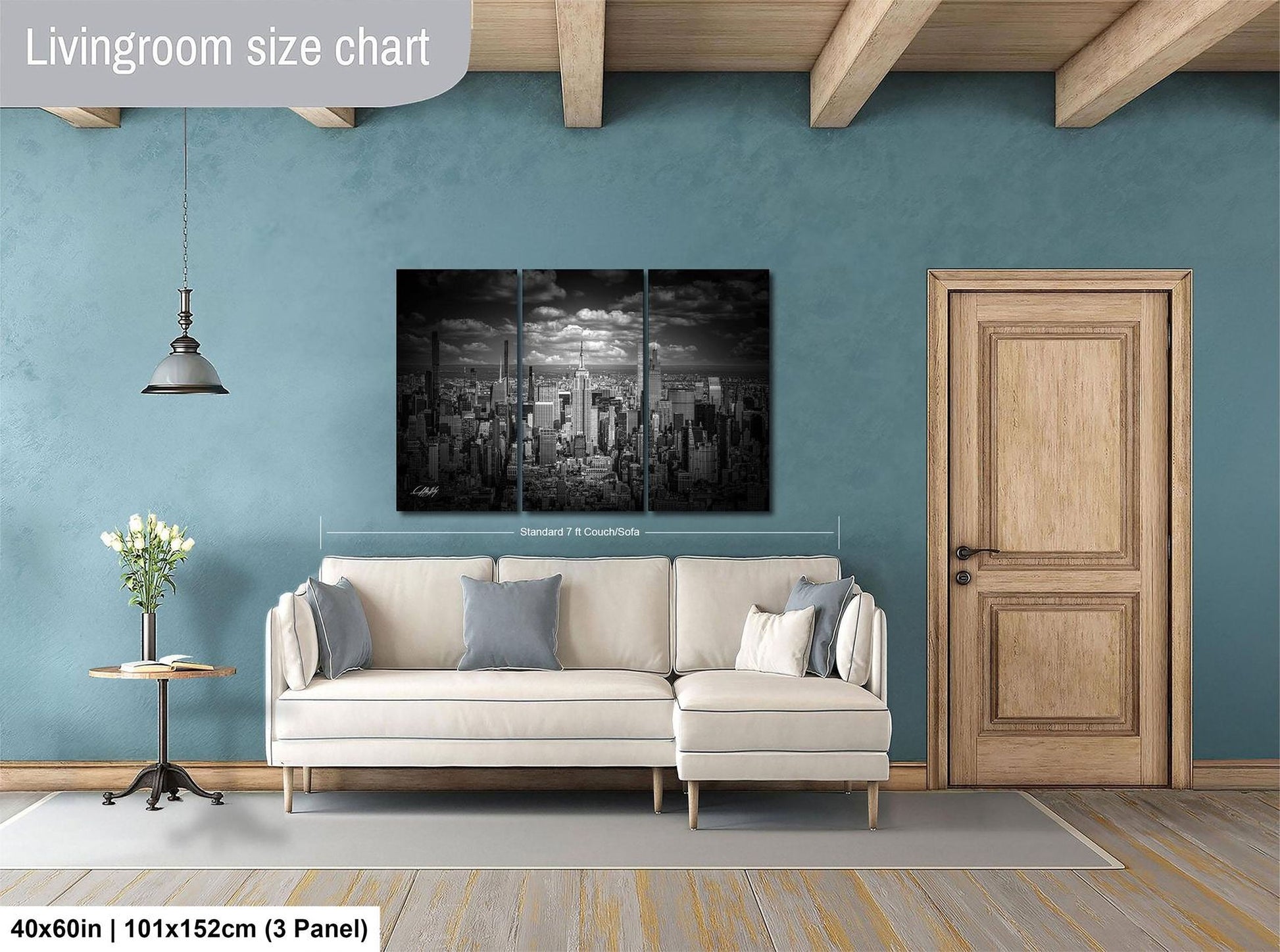 The image is a living room with a large, black and white cityscape painting hanging on the wall. The painting is divided into three panels, and the living room has a white sofa, a wooden door, and a small table with a vase of flowers.