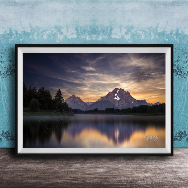 The image is a framed photograph of a serene mountain landscape at sunset, with a calm lake reflecting the vibrant colors of the sky.