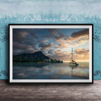 A framed photograph depicting a serene scene of a sailboat on a calm body of water, with a mountainous landscape and a colorful sunset in the background.
