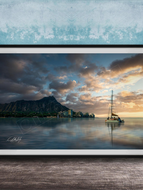 A framed photograph depicting a serene scene of a sailboat on a calm body of water, with a mountainous landscape and a colorful sunset in the background.