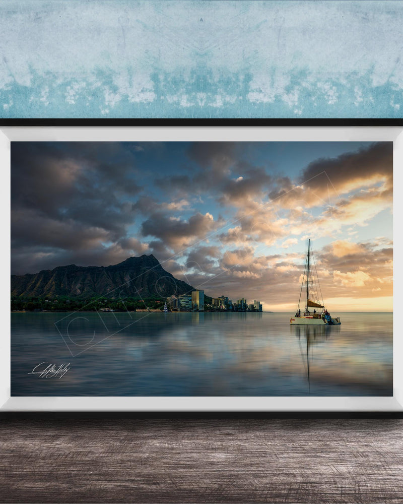 A framed photograph depicting a serene scene of a sailboat on a calm body of water, with a mountainous landscape and a colorful sunset in the background.