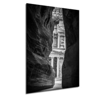 A black and white photograph of a narrow passage between two large rock formations, with a classical building visible through the opening.