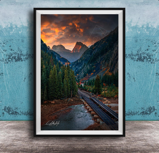 a scenic mountain landscape with a winding road, lush forests, and a dramatic sky with orange and red clouds.