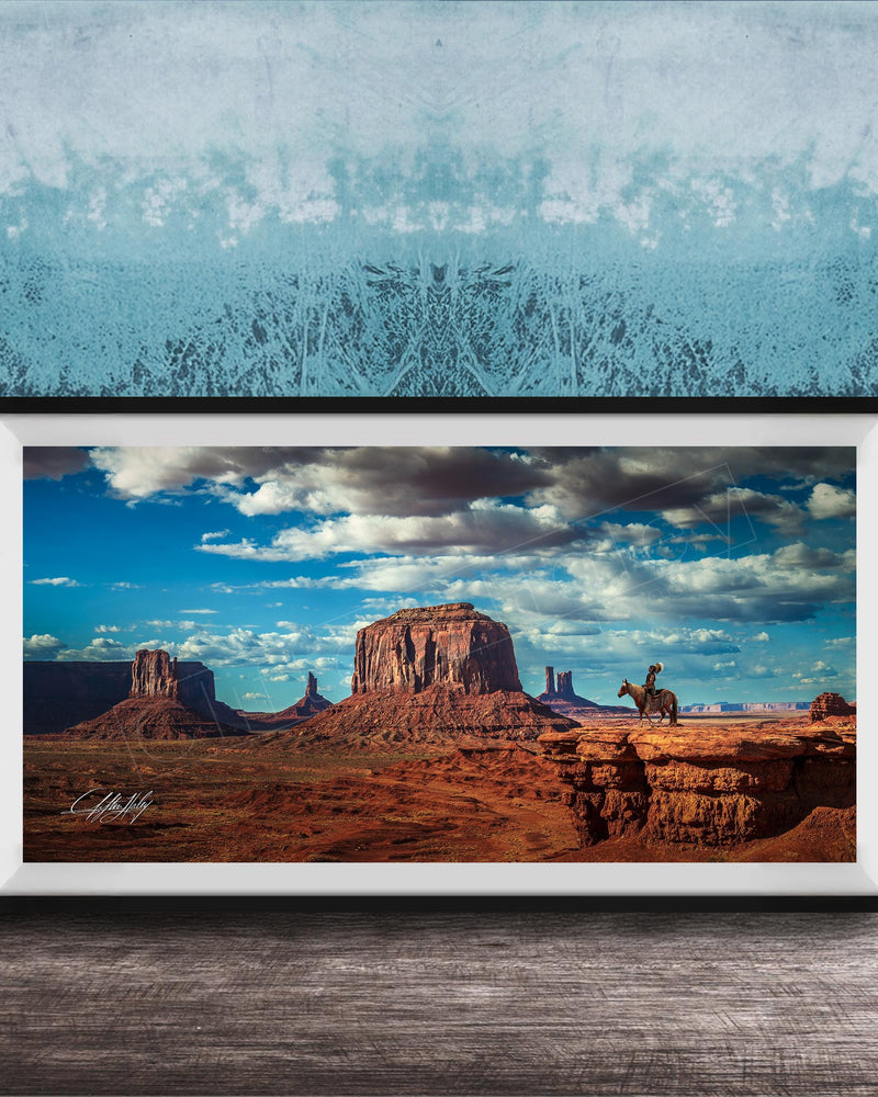 A framed photograph of a desert landscape with a cowboy on a horse, set against a blue and white patterned background.