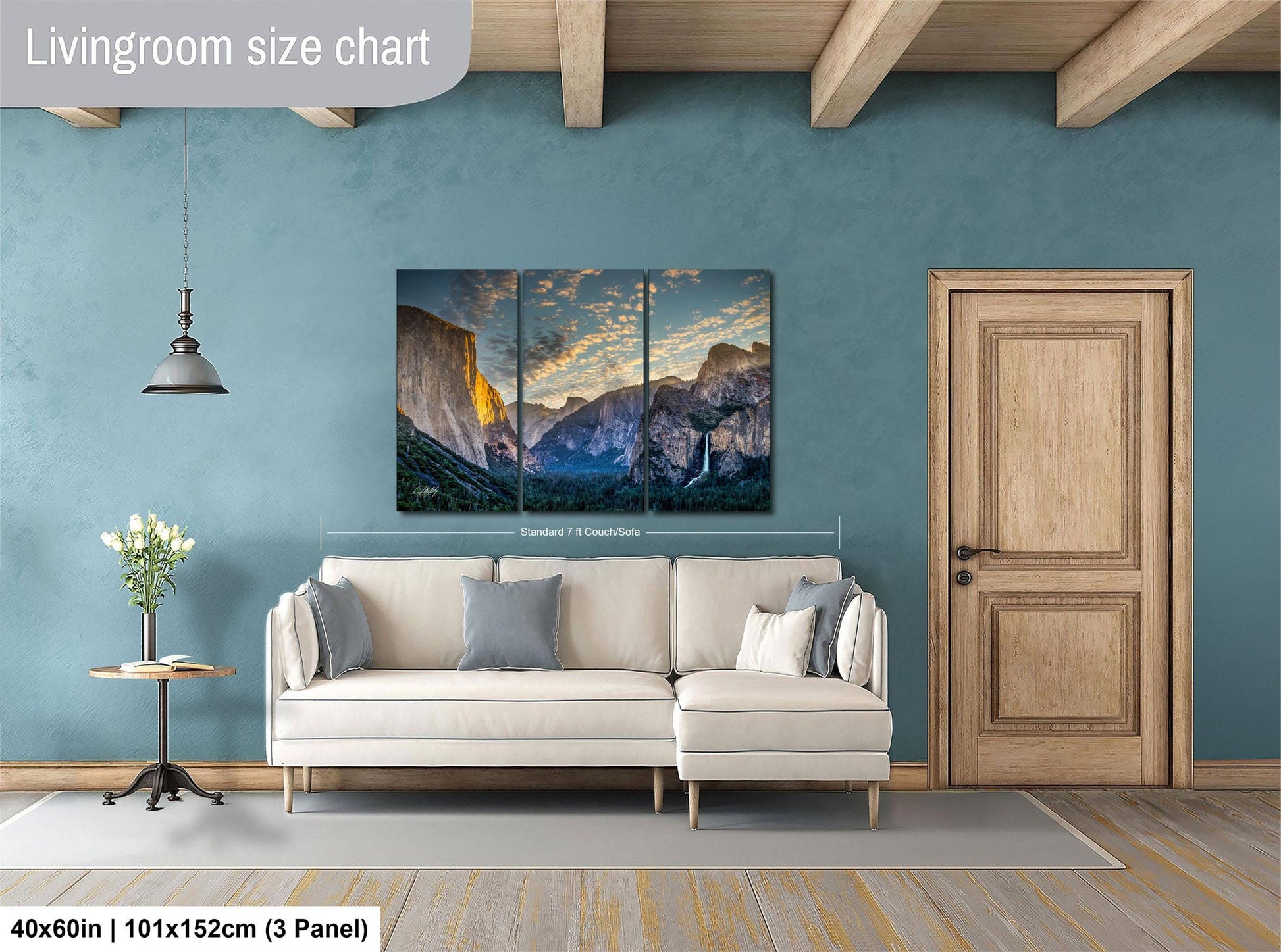 The image is a living room with a large, three-panel landscape painting hanging on the wall. The painting depicts a scenic mountain range with a sunset in the background. The room has a white sofa and a wooden door, creating a cozy and inviting atmosphere.