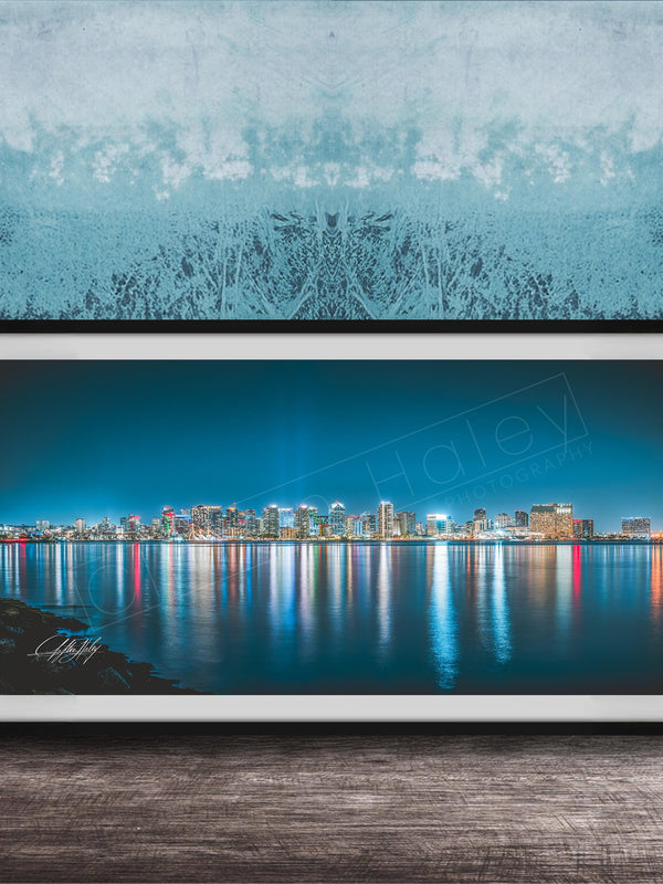 A framed photograph of a city skyline at night, with the buildings' lights reflected in the water below.