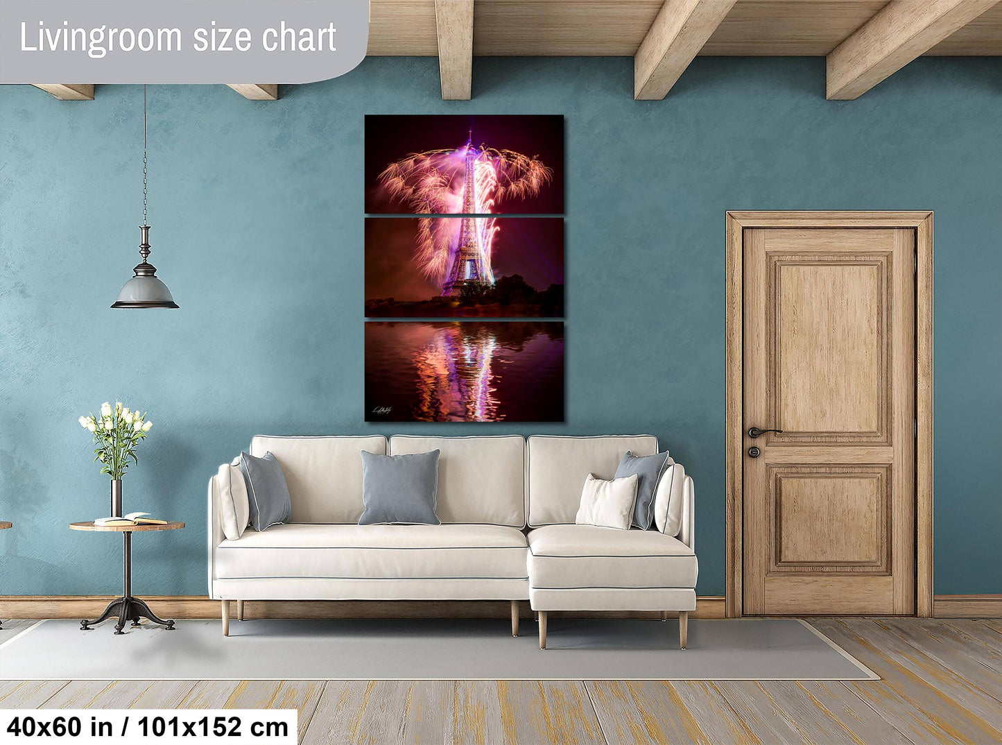 The image is a living room with a white sofa, a wooden door, and a large wall art depicting a fireworks display over the Eiffel Tower.
