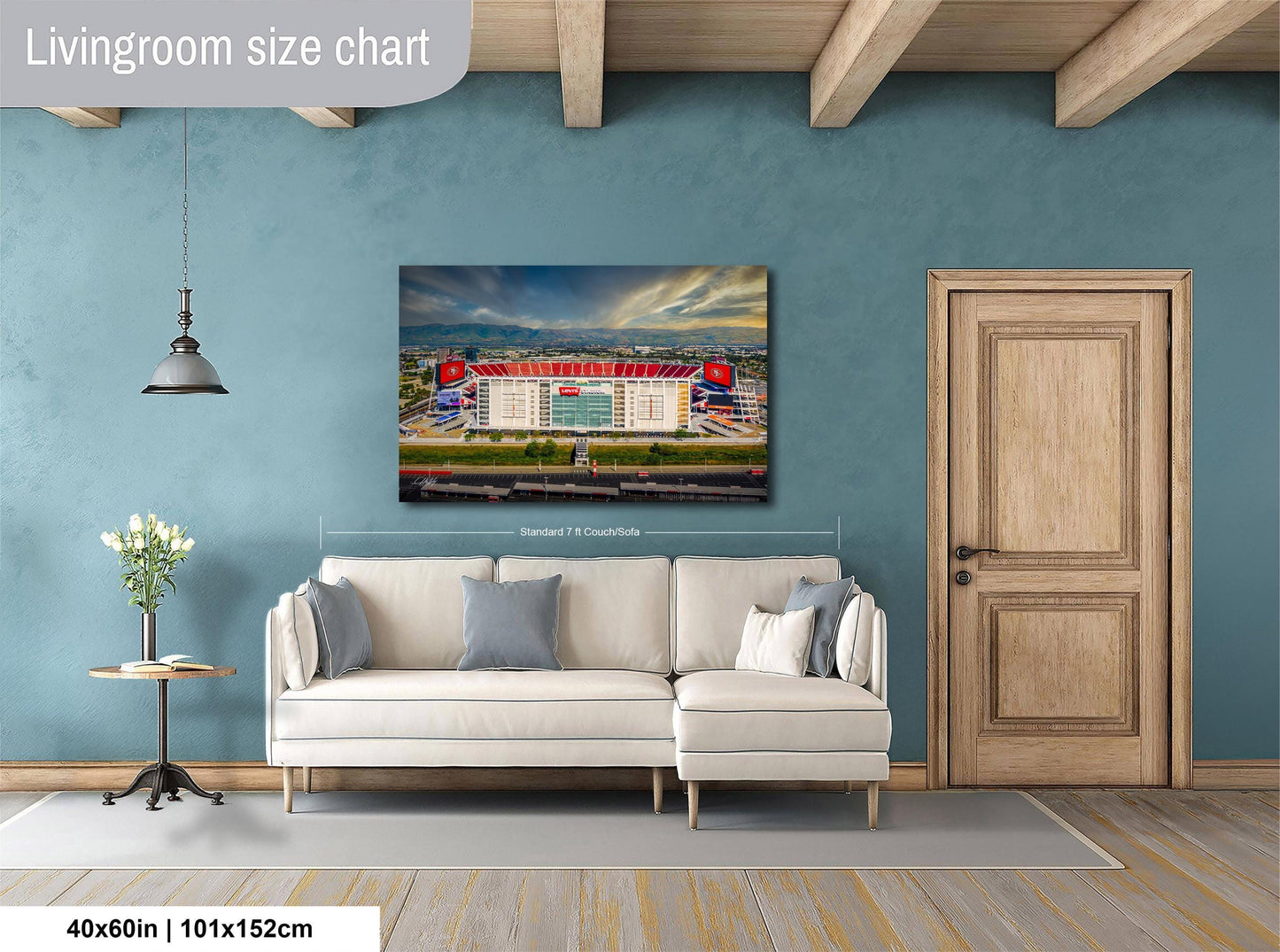 a living room with a large wall-mounted painting of a stadium, a white sofa, a wooden door, and a small table with a vase of flowers.