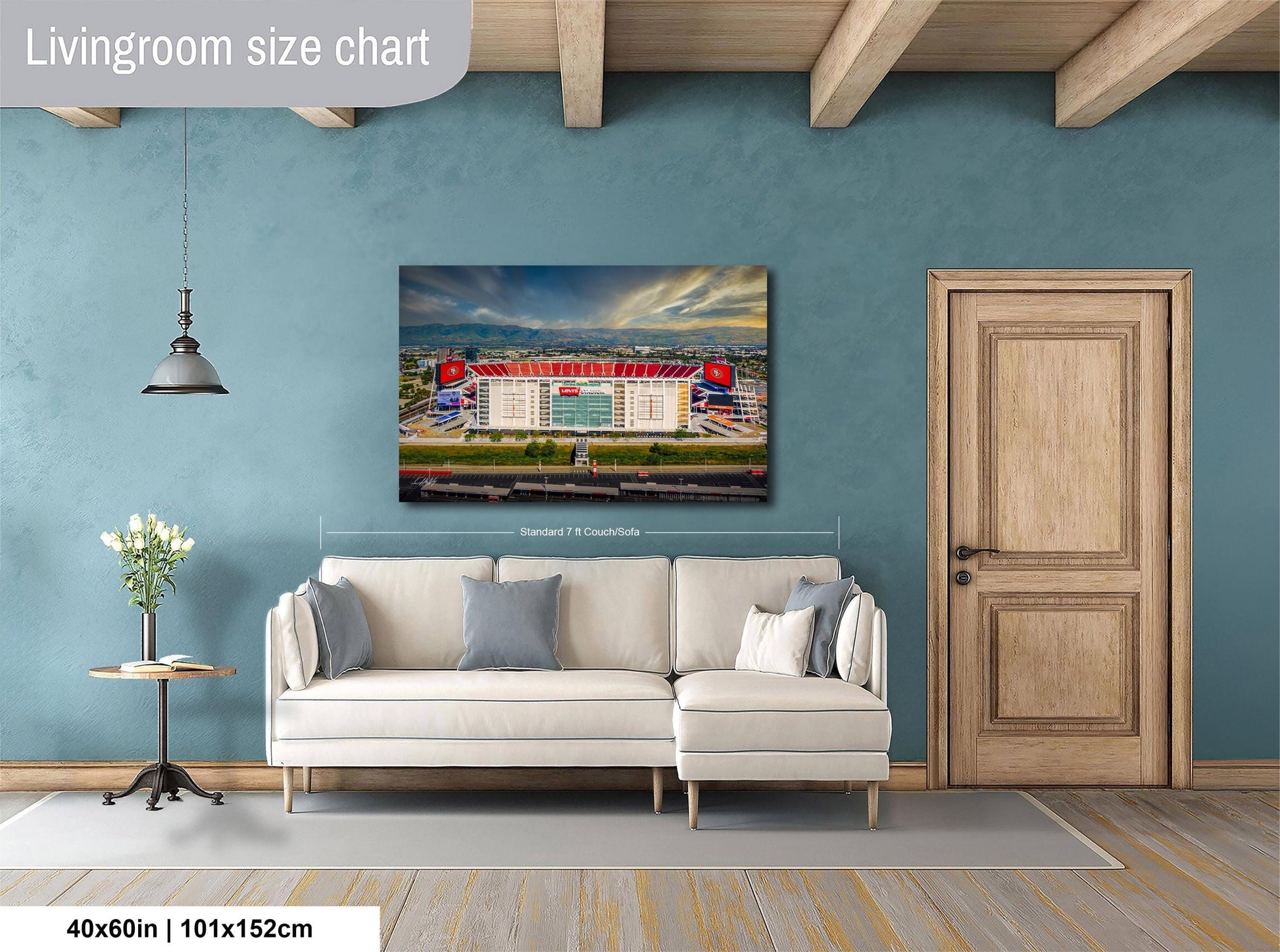 a living room with a large wall-mounted painting of a stadium, a white sofa, a wooden door, and a small table with a vase of flowers.