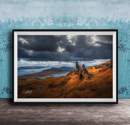 The image is a framed photograph depicting a dramatic landscape with a rocky outcrop, a lake, and a cloudy sky.