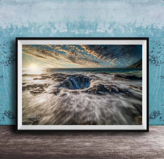 A framed photograph depicting a dramatic natural landscape with a large hole or sink in the center, surrounded by crashing waves and a vibrant sky.