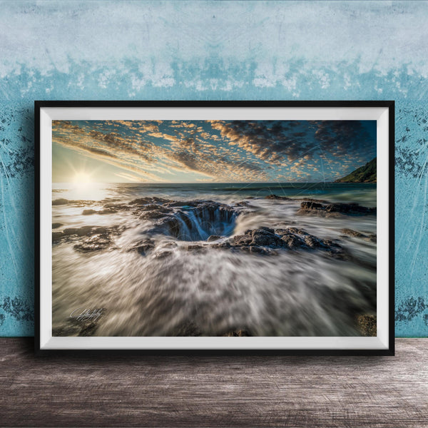 A framed photograph depicting a dramatic natural landscape with a large hole or sink in the center, surrounded by crashing waves and a vibrant sky.