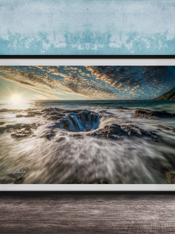 A framed photograph depicting a dramatic natural landscape with a large hole or sink in the center, surrounded by crashing waves and a vibrant sky.