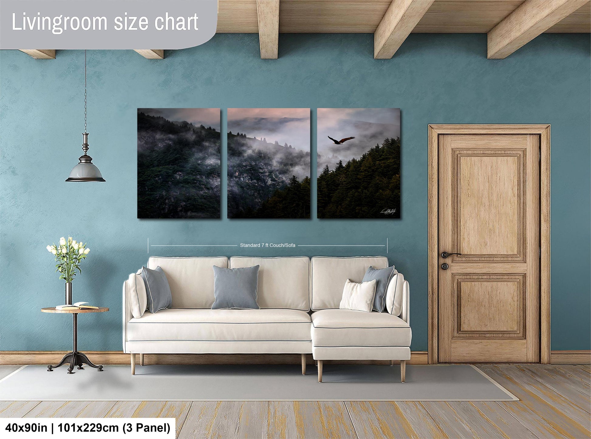 The image is a living room with a white sofa and a wooden door. Above the sofa, there is a large wall art panel depicting a forest scene with a bird flying over the trees. The wall art is framed by a wooden border and is approximately 40 inches wide and 101.29 cm in height.