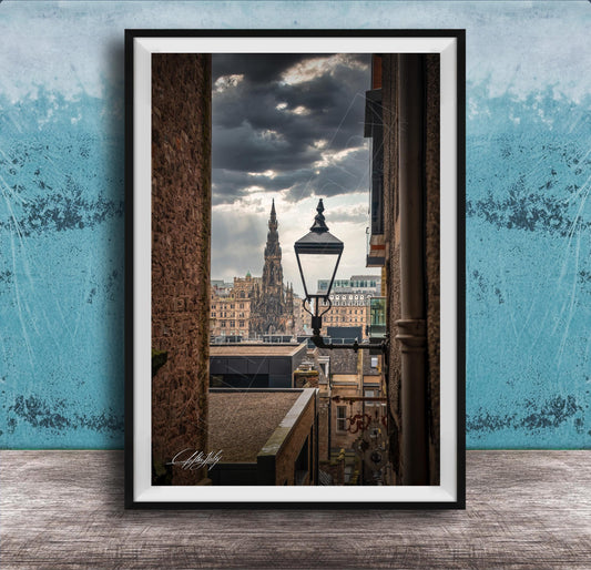 a cityscape with a tall, ornate building in the background, framed in a black frame and placed on a wooden surface against a blue wall.