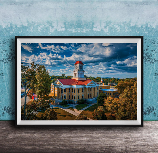 A framed photograph of a large, ornate building with a red roof and a clock tower, surrounded by trees and a blue sky with clouds.