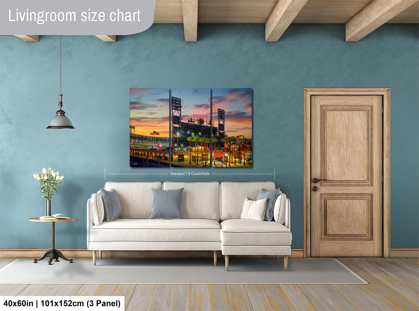 The image is a living room with a large, colorful painting of a baseball stadium hanging on the wall. The painting is divided into three panels, depicting the stadium and its surroundings. The room has a white sofa and a wooden door, creating a cozy and inviting atmosphere.
