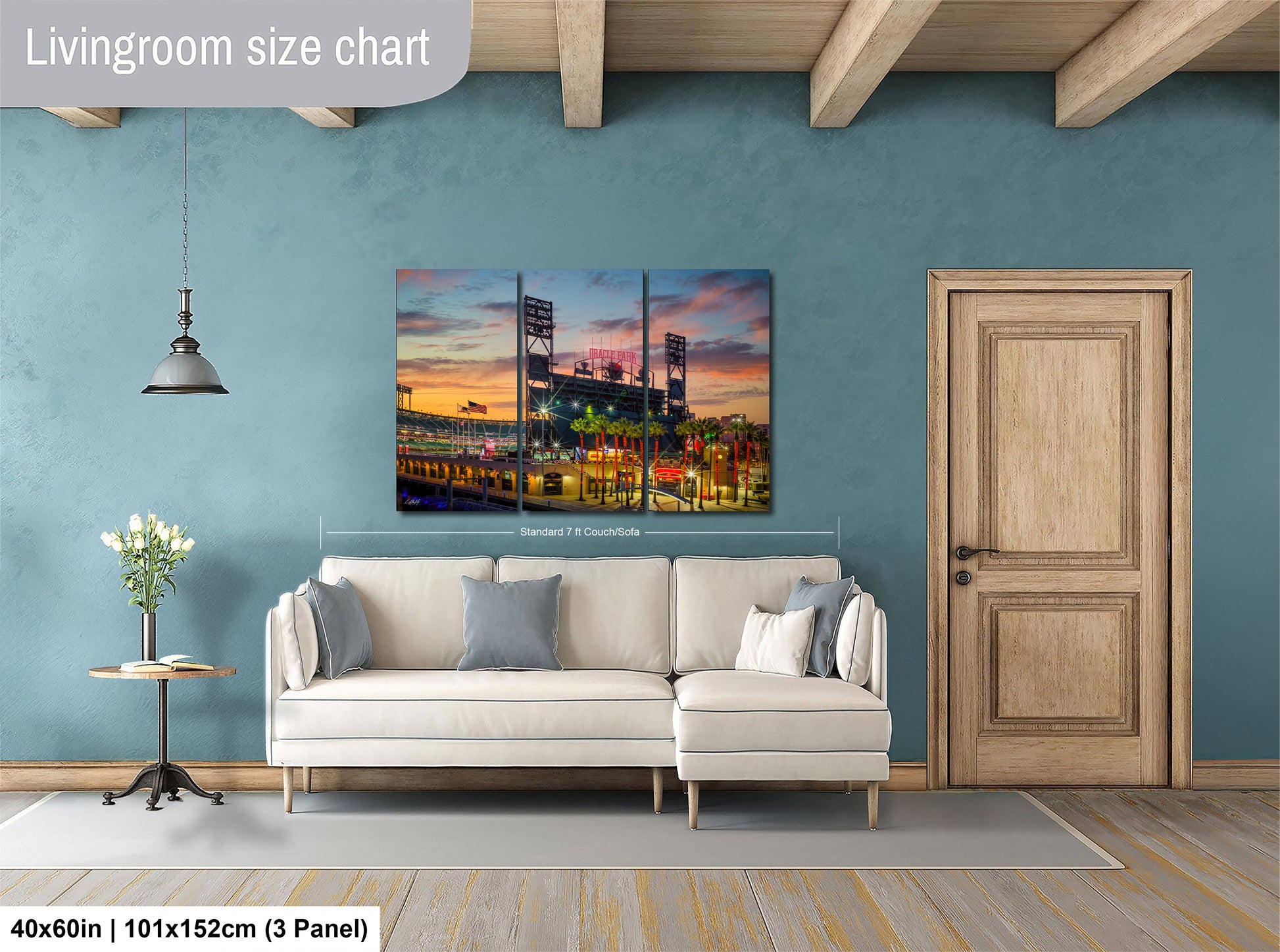 The image is a living room with a large, colorful painting of a baseball stadium hanging on the wall. The painting is divided into three panels, depicting the stadium and its surroundings. The room has a white sofa and a wooden door, creating a cozy and inviting atmosphere.