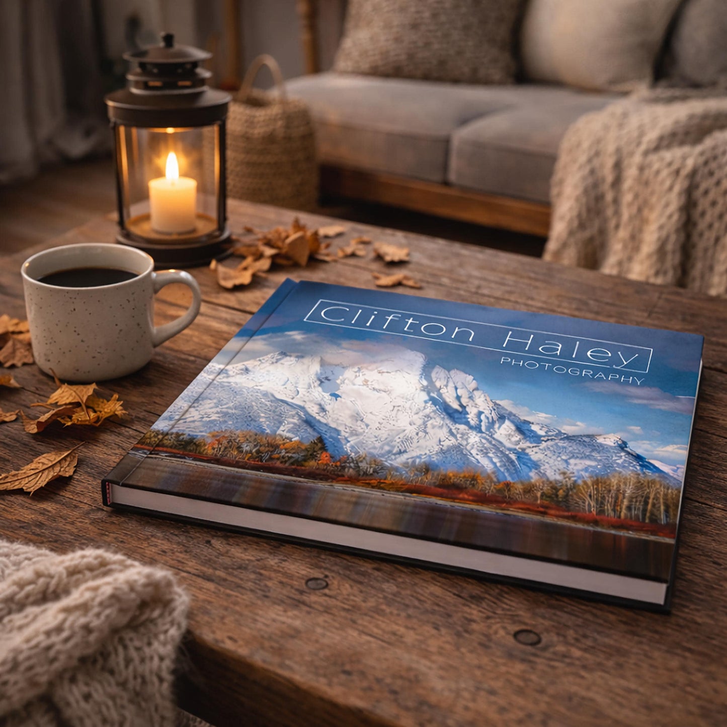a wooden coffee table with a book titled "Clifton Haley Photography" on it, along with a lit candle, a mug of coffee, and some fallen leaves.