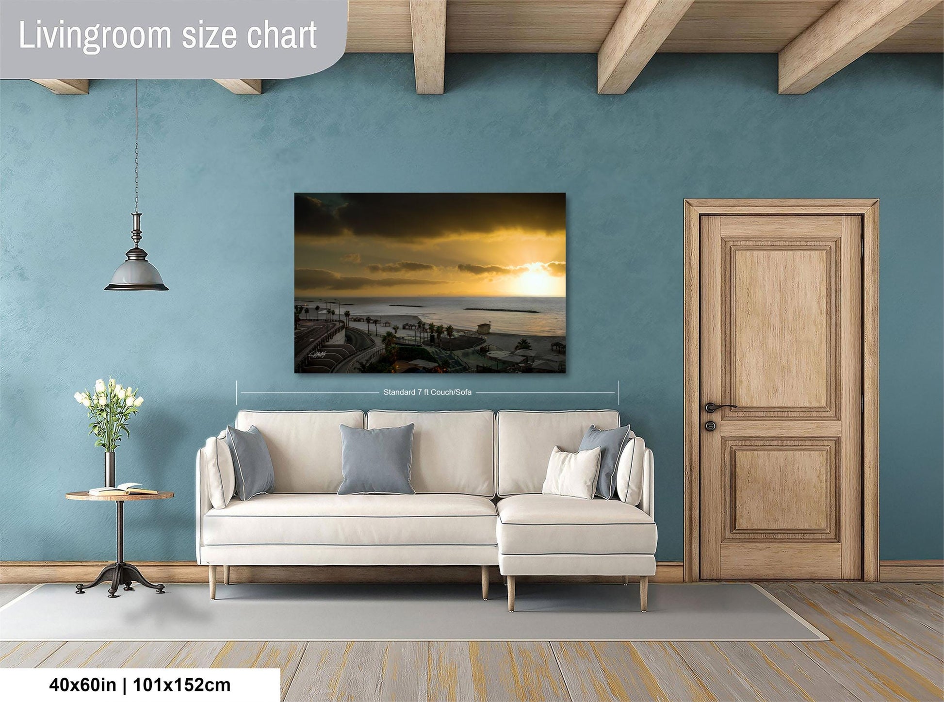 a living room with a large painting of a sunset over the ocean hanging on the wall. The painting is framed and measures 40 inches by 101.5 centimeters. The room has a white sofa, a wooden door, and a small table with a vase of flowers.