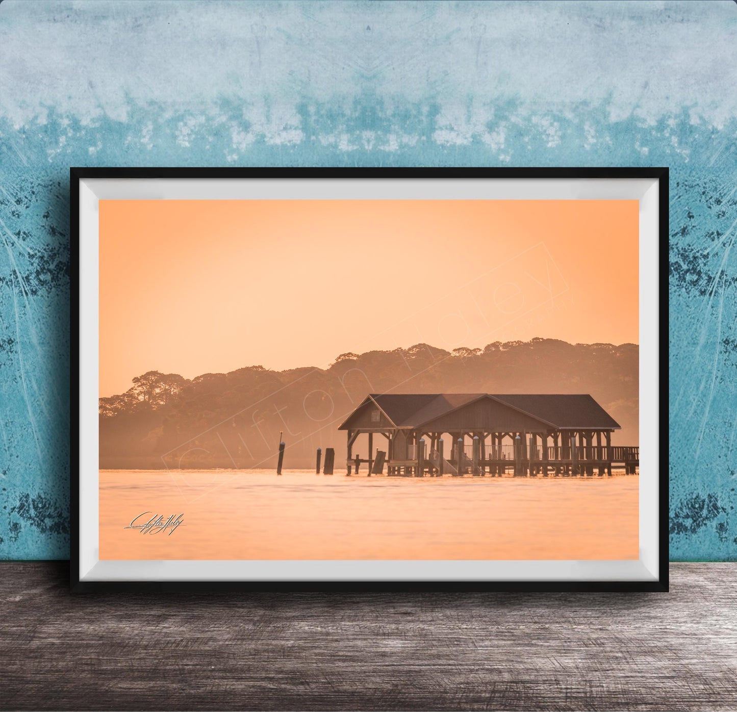 A framed photograph of a wooden pier extending into a body of water, with a warm orange and yellow sunset sky in the background.