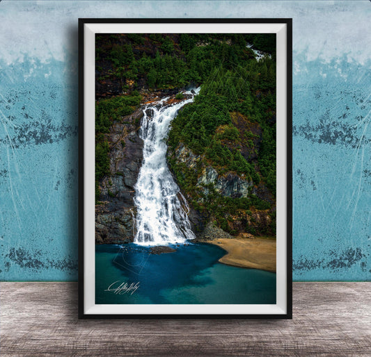 A framed photograph of a waterfall cascading down a rocky cliff surrounded by lush greenery, with a blue-green body of water below.