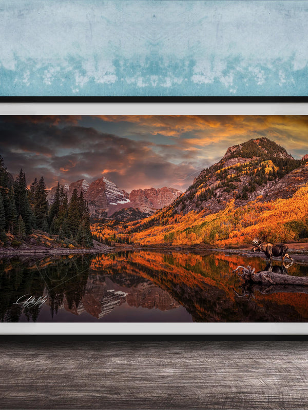 The image is a framed photograph depicting a serene mountain landscape with a lake, trees, and mountains in the background, reflecting the vibrant colors of the sky.