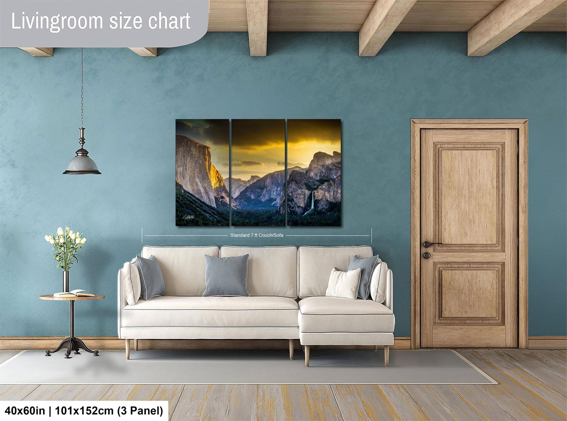 The image is a living room with a large, three-panel landscape painting hanging on the wall. The painting depicts a mountainous scene with a sunset in the background. The room has a white sofa and a wooden door, and there is a vase of flowers on a table. The painting is approximately 40 inches wide and 101.5 inches tall, with a 3-panel layout.