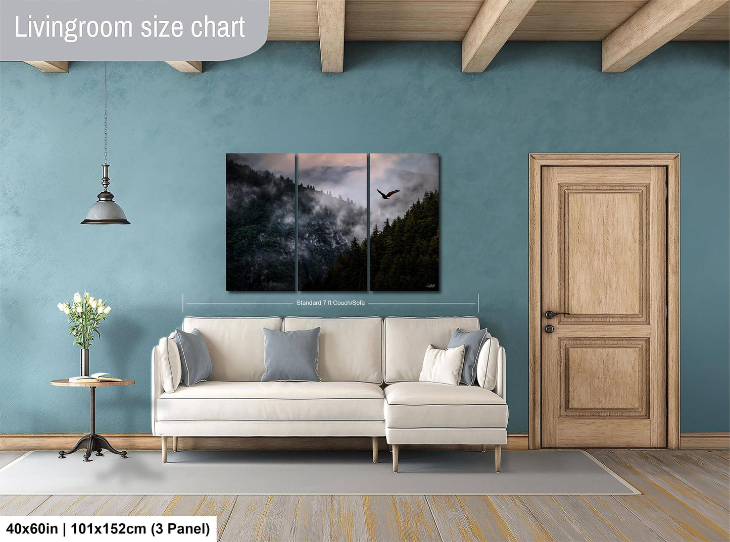 The image is a living room with a large white sofa, a wooden door, and a painting of a forest scene above it. The painting is a triptych, with the top and bottom panels depicting a mountain landscape with a bird in flight. The wall behind the sofa is painted a light blue color, and there is a wooden table with a vase of flowers on it. The image is described as a living room size chart, indicating that it is a scale model or a representation of the actual room.