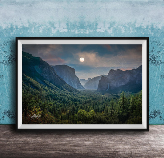 The image is a framed photograph of a mountainous landscape with a full moon in the sky, surrounded by trees and forests.