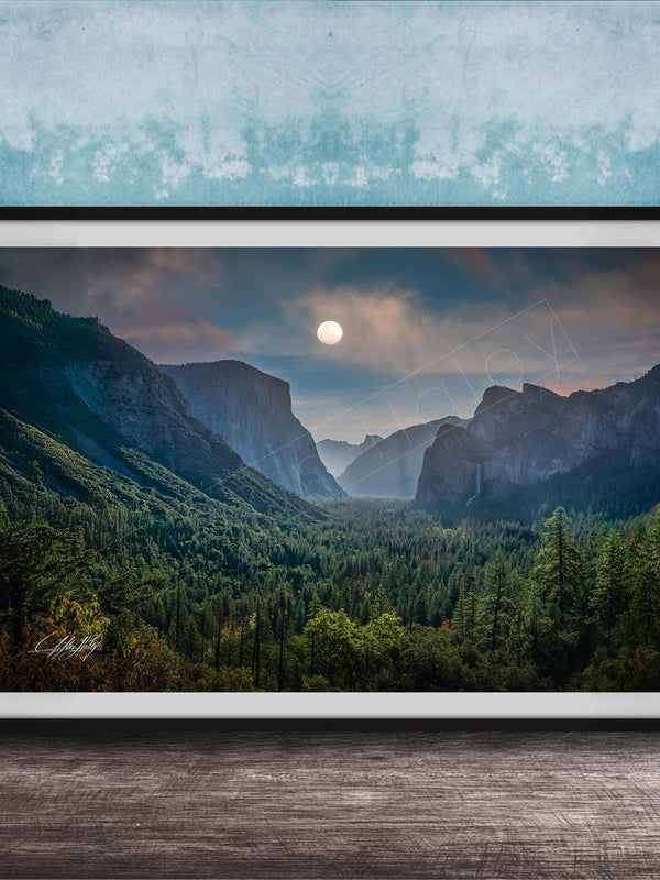 The image is a framed photograph of a mountainous landscape with a full moon in the sky, surrounded by trees and forests.
