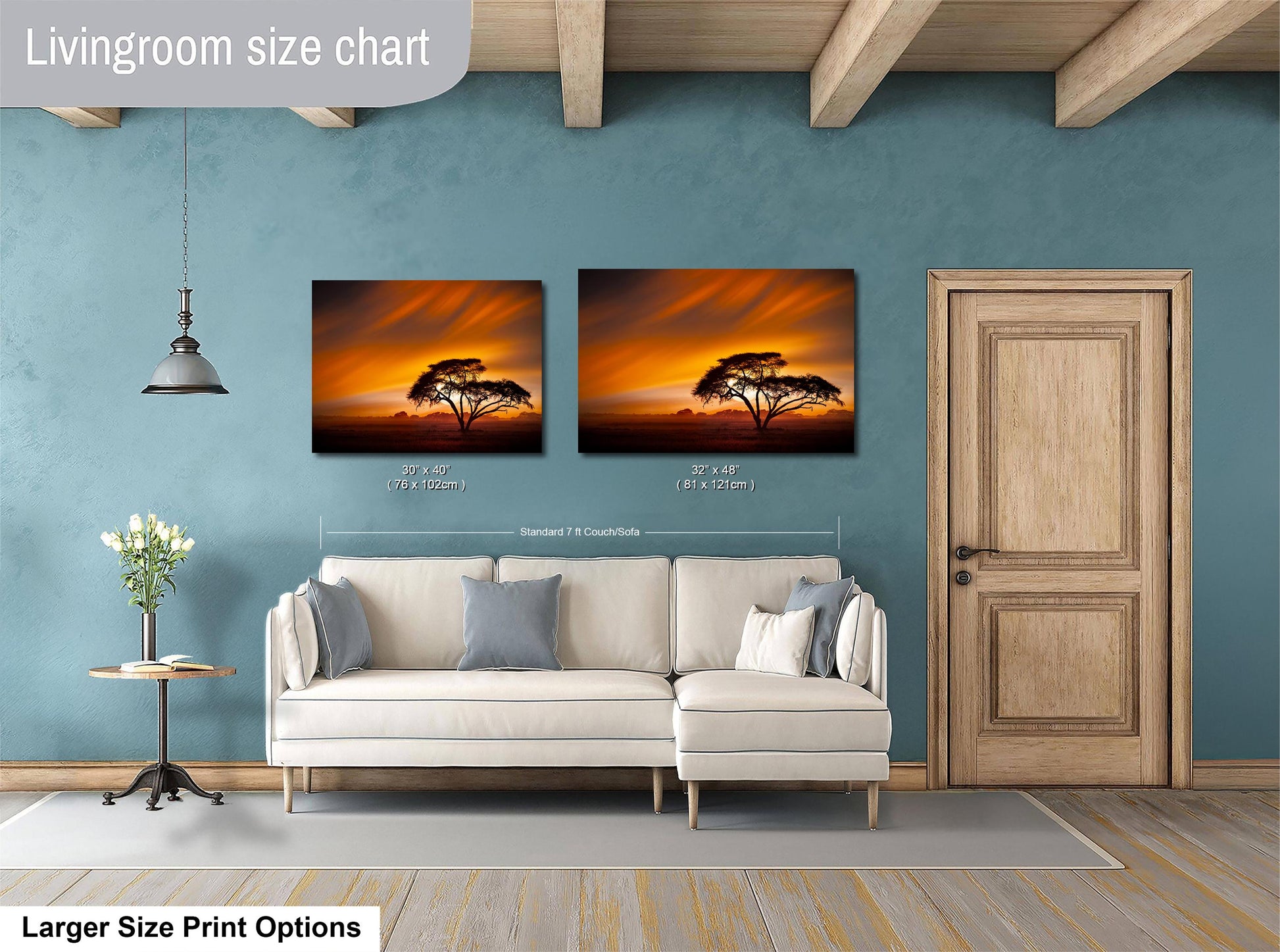 a living room with a white sofa and a wooden door. Above the sofa, there are two framed pictures of a tree against a sunset background. The living room has a blue wall and a wooden ceiling.